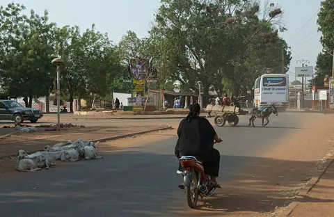 Koutiala, Mali — 2014.04-416-330aS scenery(urban),sheep,traffic,motorbike,donkey cart,bus Koutiala(Sikasso Rgn),ML sun13apr2014-0831h